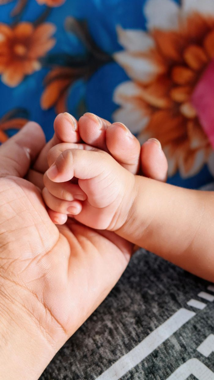 An intimate scene of an adult and baby holding hands, symbolizing care.