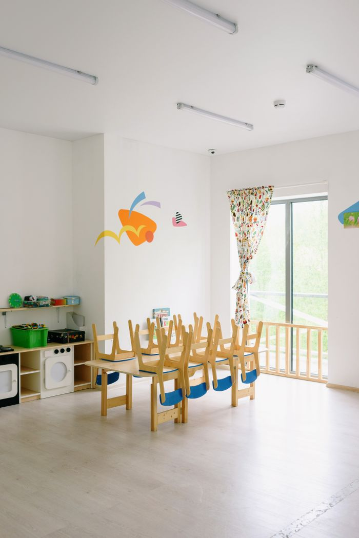 Spacious and bright kindergarten classroom with child-sized wooden furniture and playful decor.